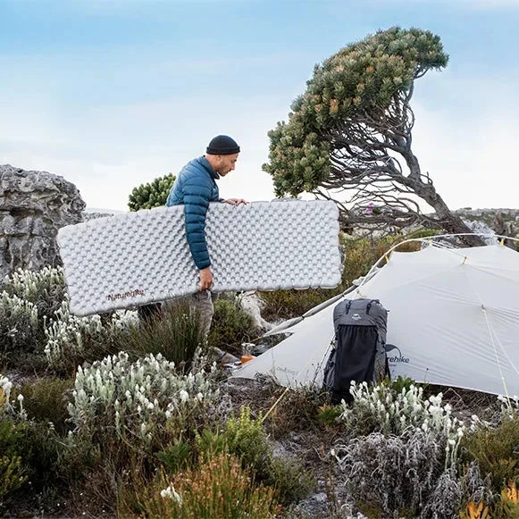 person carrying a sleeping pad towards a tent outdoors