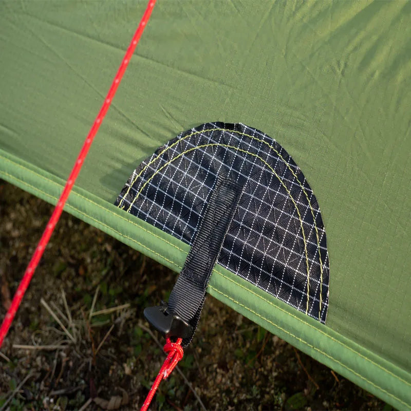 Close-up of a green tent with a black strap and red rope on a grassy background