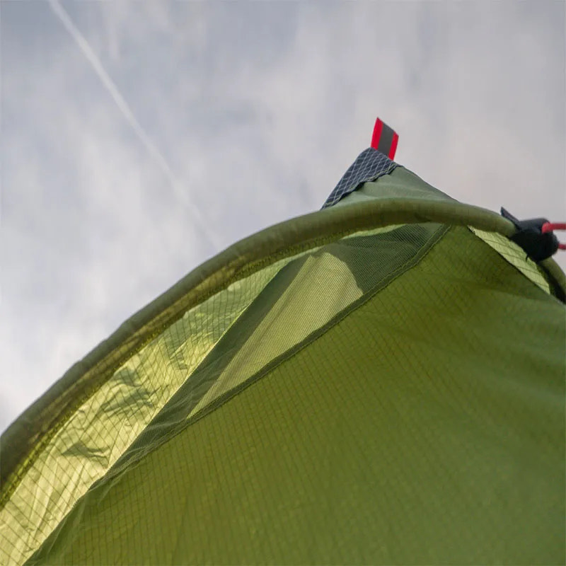 Close-up of a green tent with a red and black component against a cloudy sky.