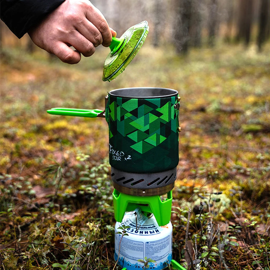 Person using a portable camping stove with a green geometric pattern in a forest setting.