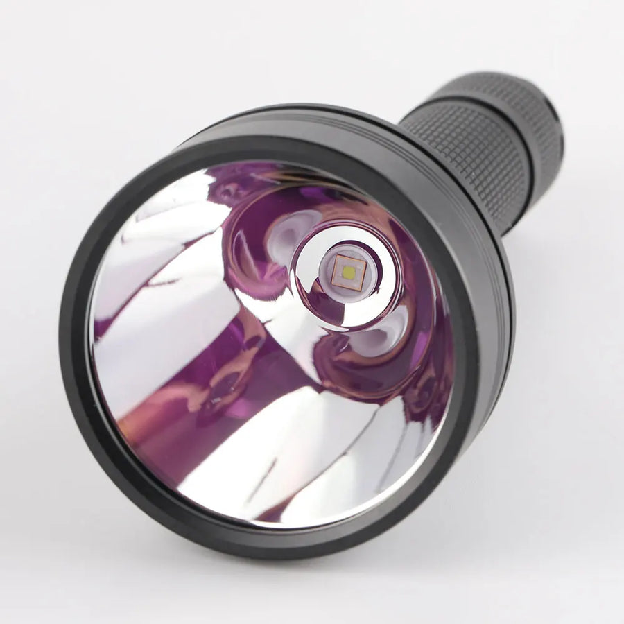 Close-up of a flashlight lens with purple reflective coating on a white background