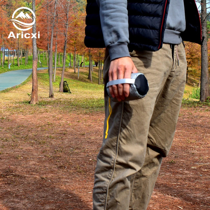 Person wearing a puffer jacket and cargo pants in a park setting with 'Aricxi' branding.