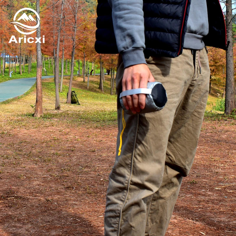 Person wearing a puffer jacket and cargo pants in a park setting with 'Aricxi' branding.