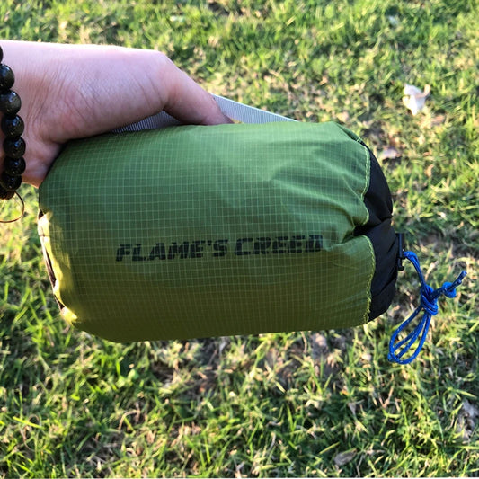 Green stuff sac with 'Flame's Creed' branding held by a person on grass.