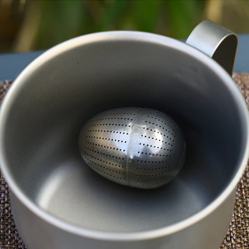 Metallic tea infuser in a white mug with a blurred natural background