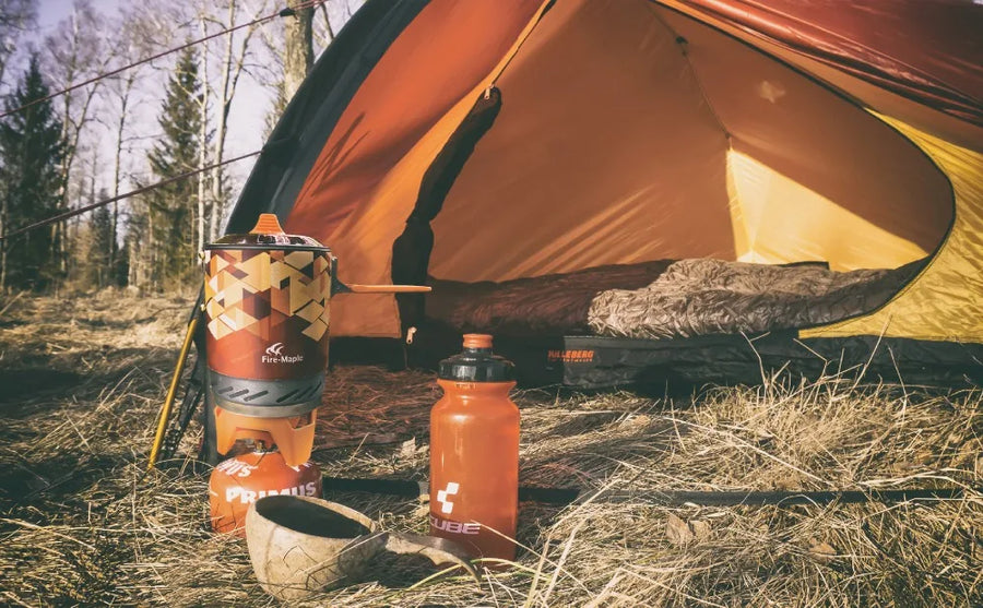 Camping scene with a tent, water bottles, and a cup in a forest setting.