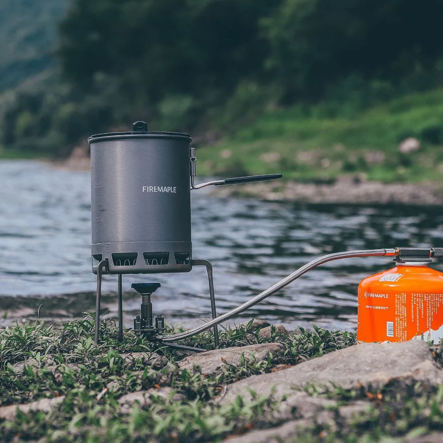 Portable camping stove with pot on a grassy area by a body of water