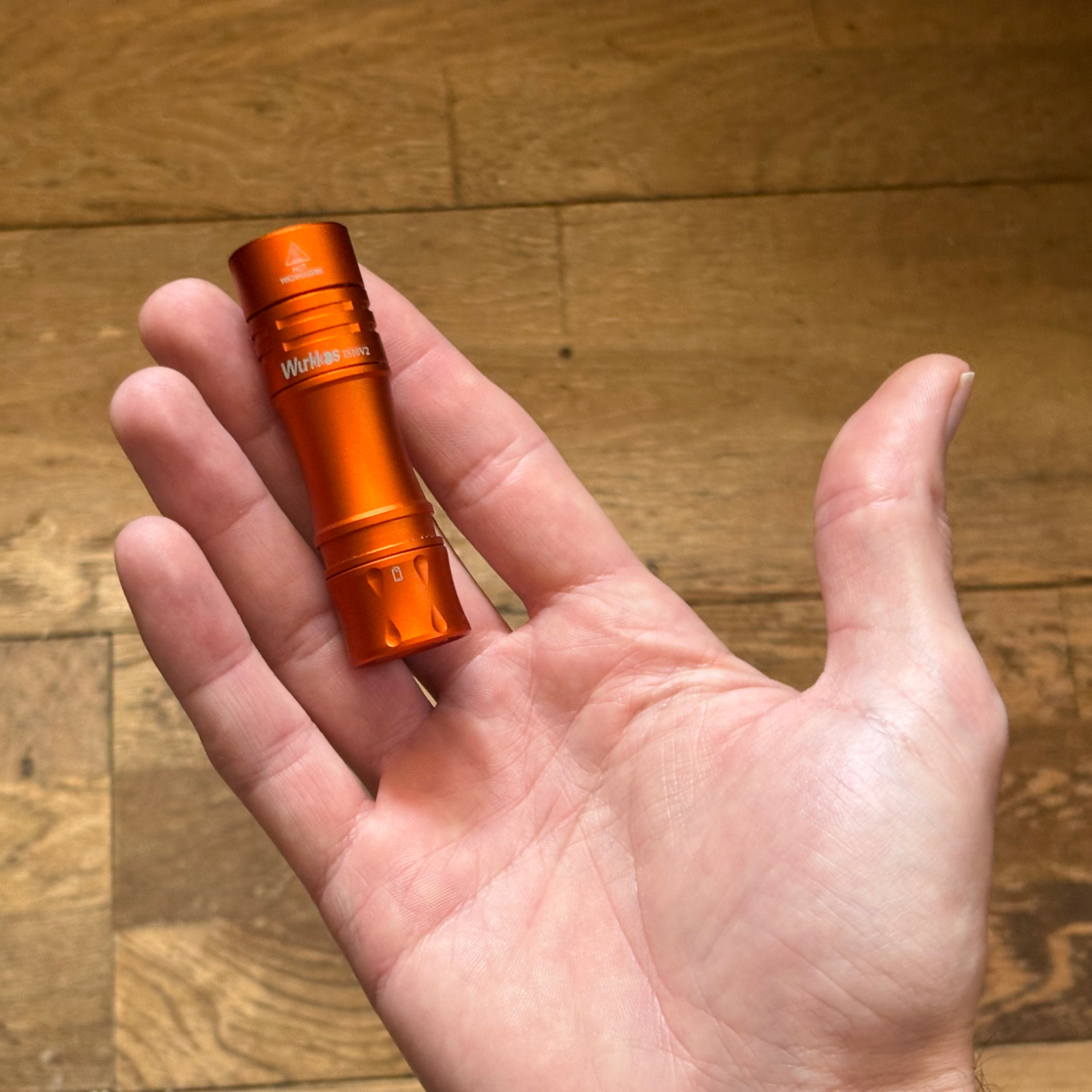 Orange flashlight held in a hand on a wooden floor