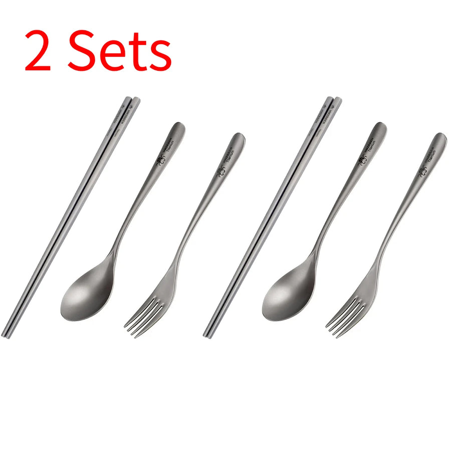 Two sets of titanium cutlery including spoons and forks on a white background.