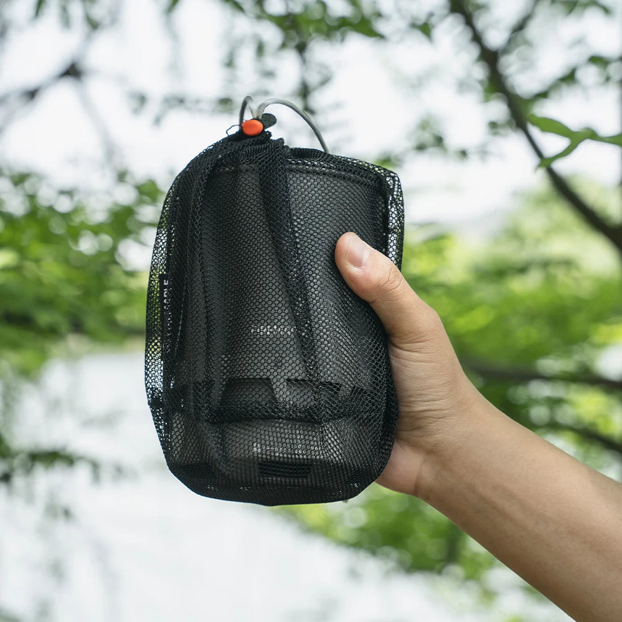 Hand holding a black mesh pouch with a blurred natural background