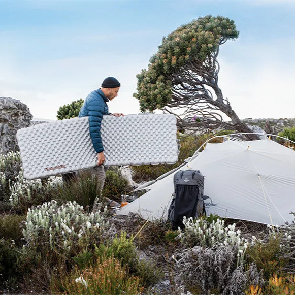 Person setting up a tent in a mountainous area with a clear sky.