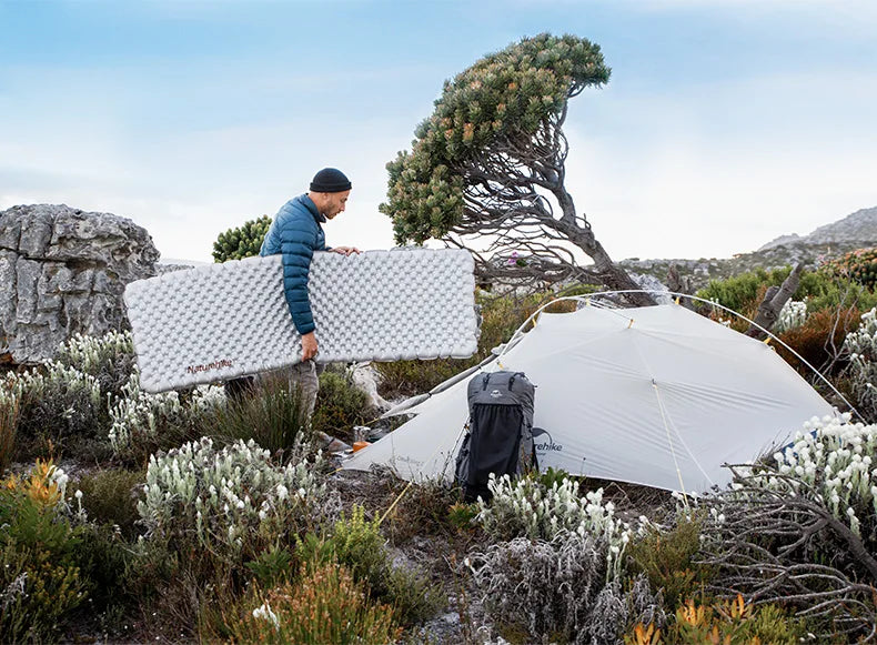 Person setting up a tent in a mountainous area with a clear sky.