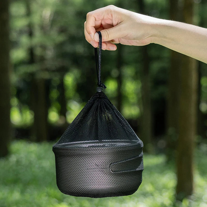 Black mesh bag held by a hand with a blurred green forest background