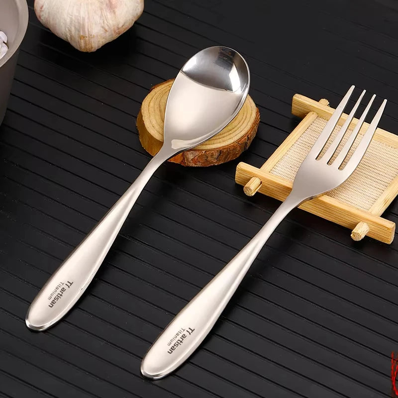 A polished titanium spoon and fork placed on a wooden board with a lemon and garlic in the background.