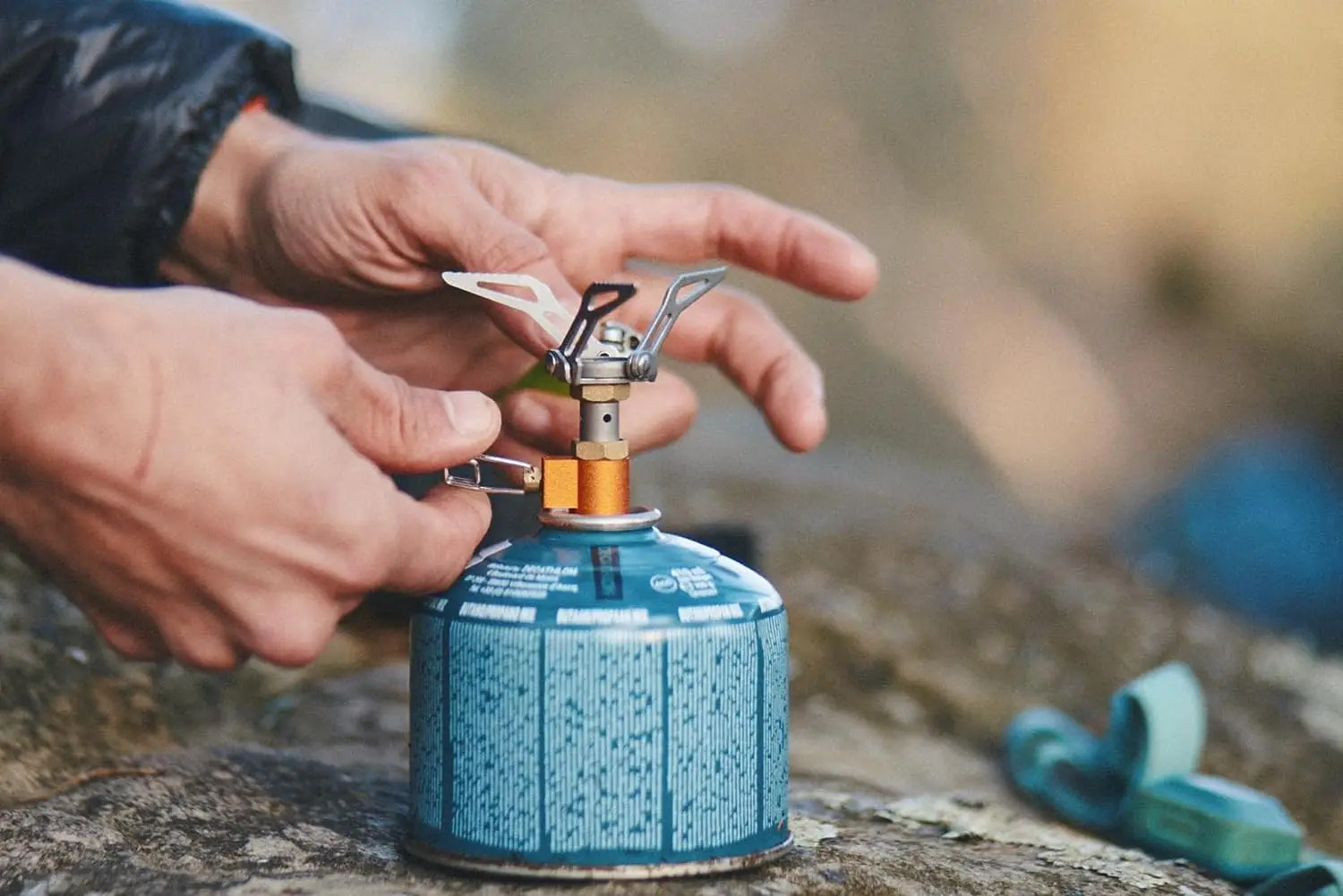 Person adjusting a blue camping stove on a natural background