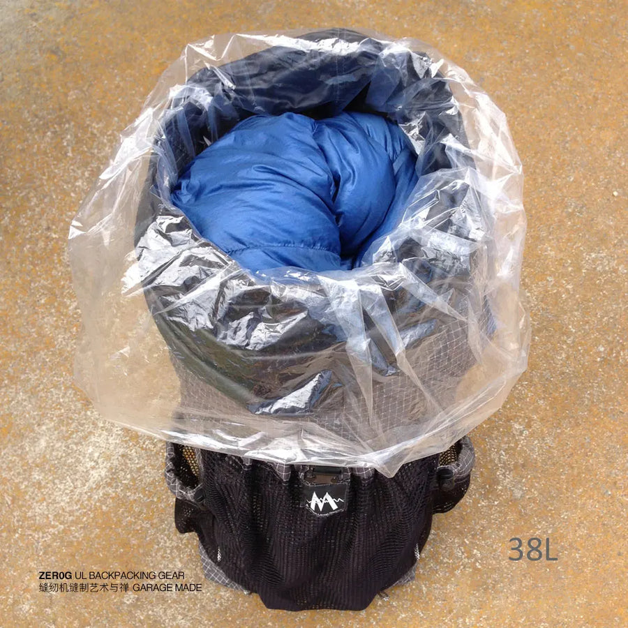 Black backpack with blue sleeping bag inside, covered by a clear plastic bag on a beige surface.