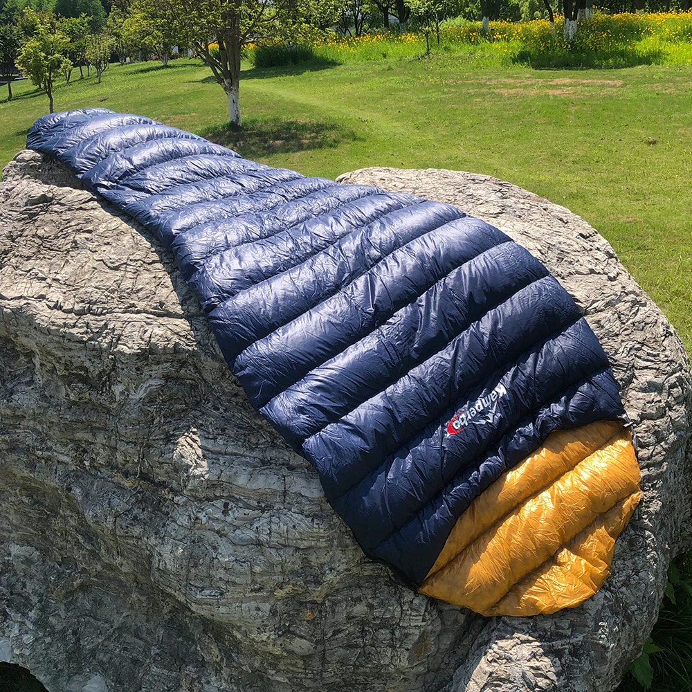 Blue and yellow sleeping bag on a rock with a grassy field in the background