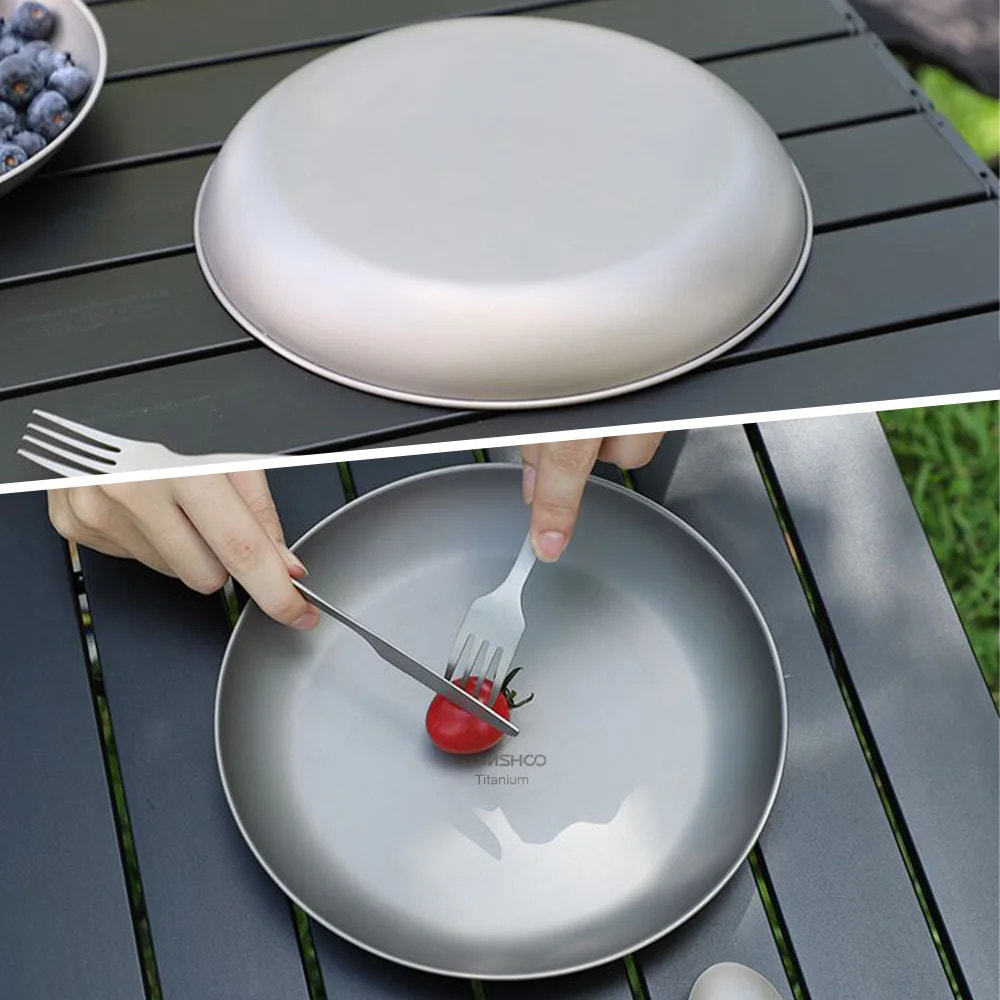 titanium plate on a wooden table with a hand using a fork and knife to cut a tomato.