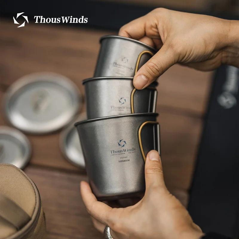Stack of ThousWinds titanium cups held by a person on a wooden surface.