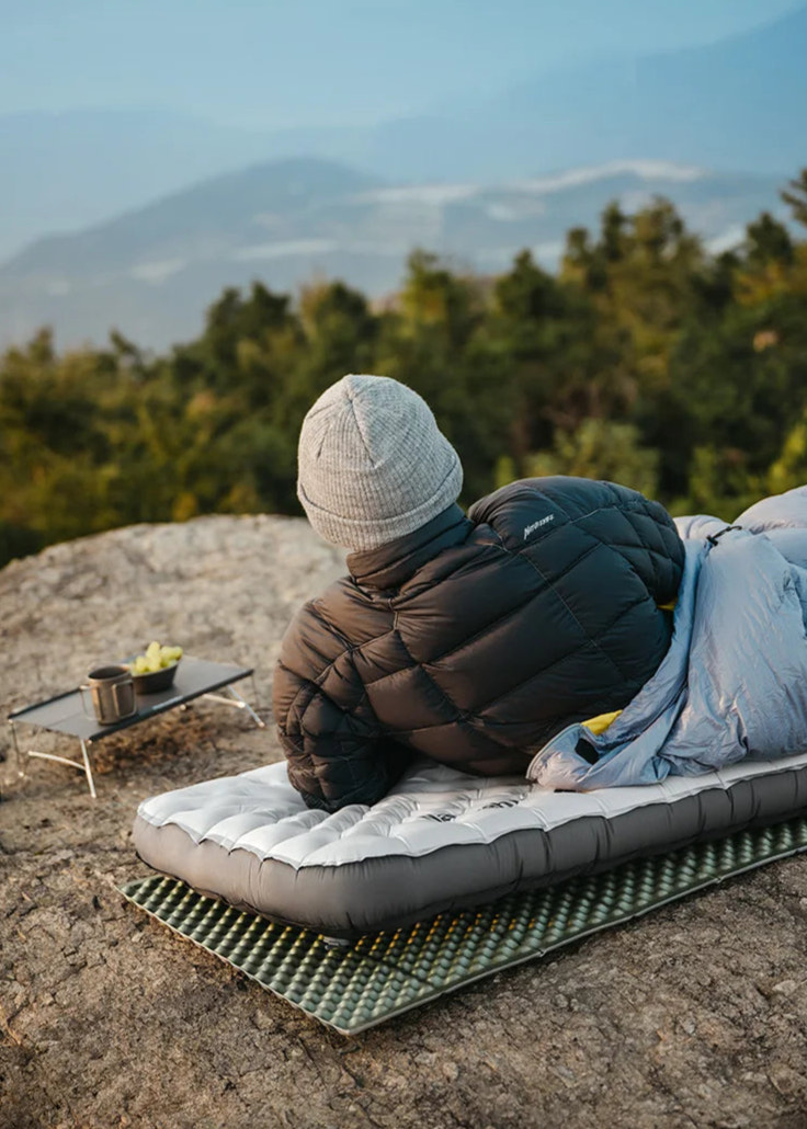 Person sitting on a camping mat with a scenic mountain view