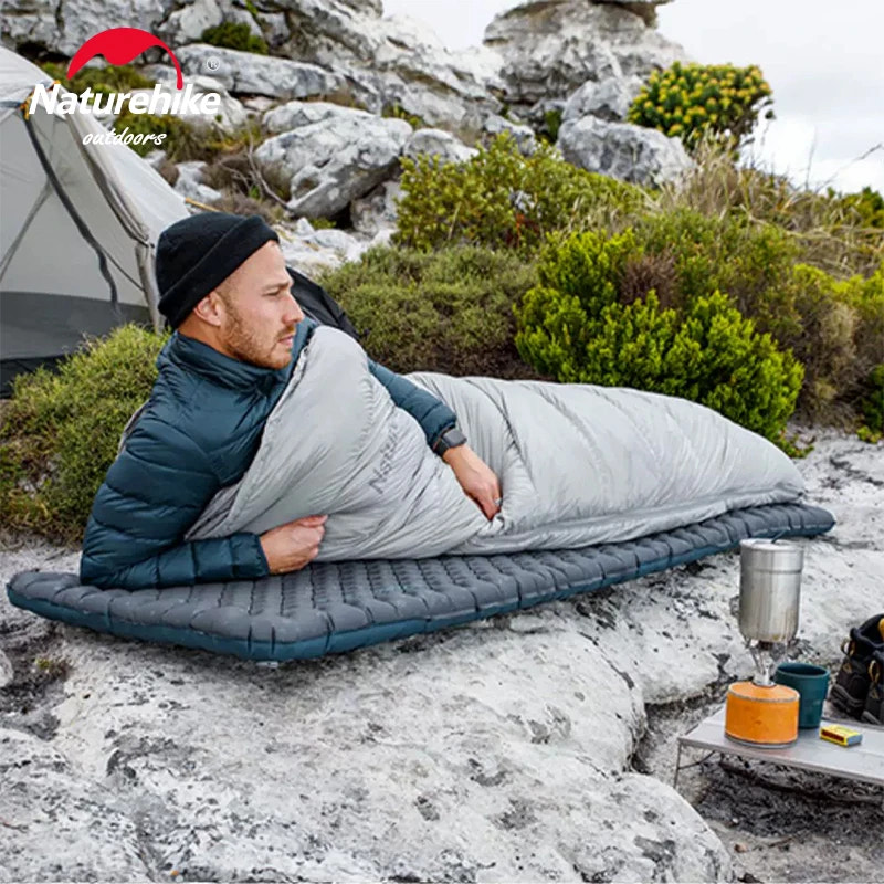 Person using a sleeping bag outdoors with Naturehike branding.