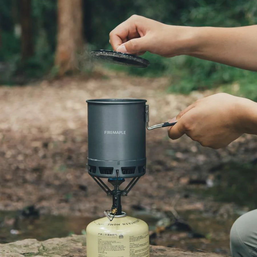 Person using a Firemaple camping stove outdoors with a blurred natural background