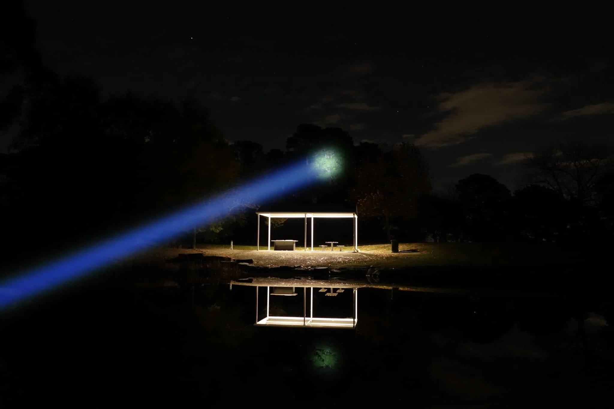 Laser pointer emitting a blue beam towards a small structure on a reflective surface at night.