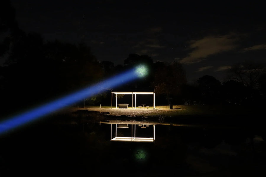 Laser pointer emitting a blue beam towards a small structure on a reflective surface at night.