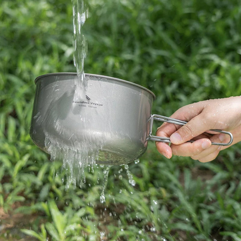 Person holding a metal pot over green foliage, with water being poured into it.