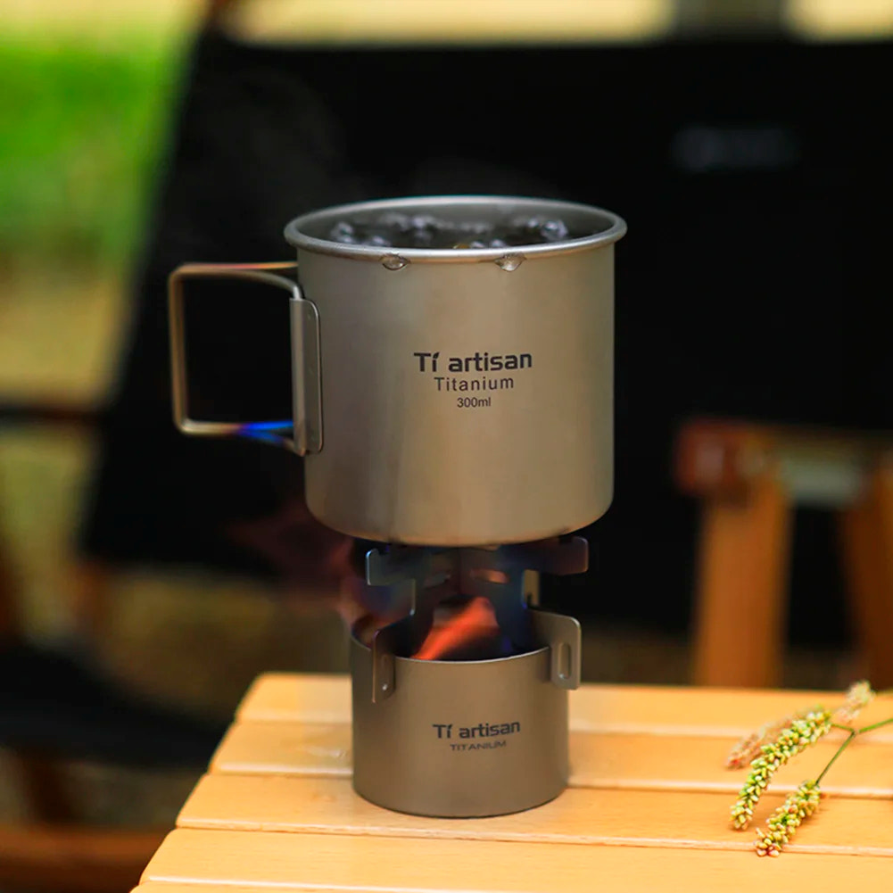 Titanium camping stove with mug on a wooden surface, blurred background