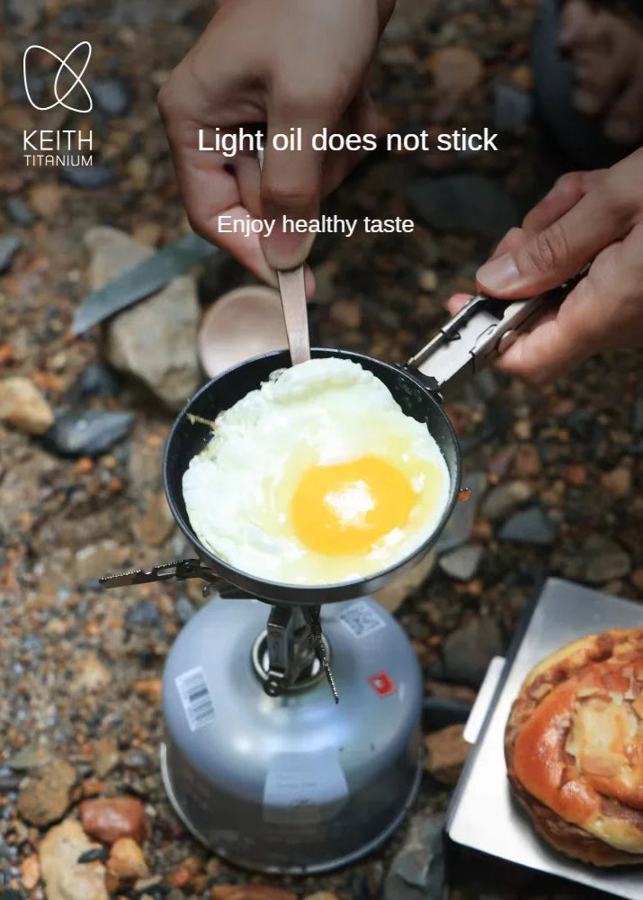 Person cooking an egg on a portable stove with Keith Titanium branding.