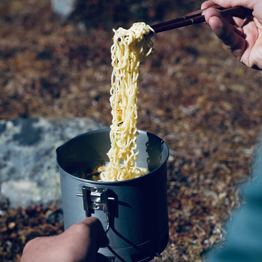 Person cooking instant noodles in a portable stove outdoors