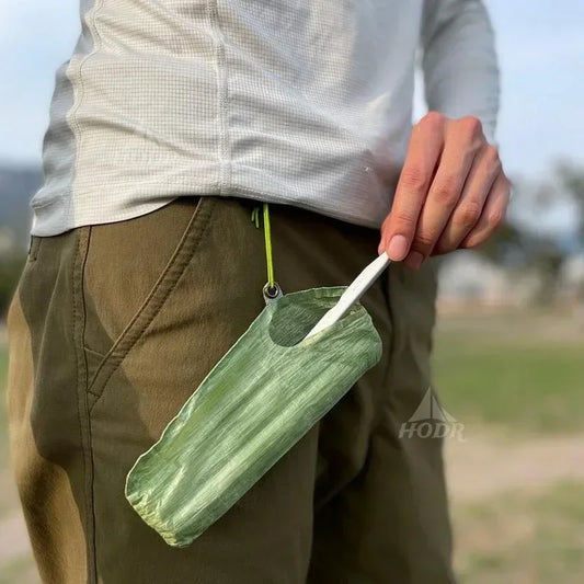 Person holding a green fabric pouch with a tent stake, outdoors.
