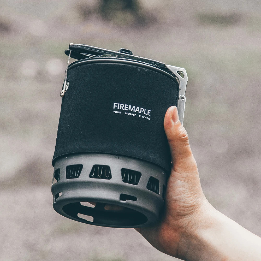 Hand holding a Firemaple portable stove against a blurred natural background