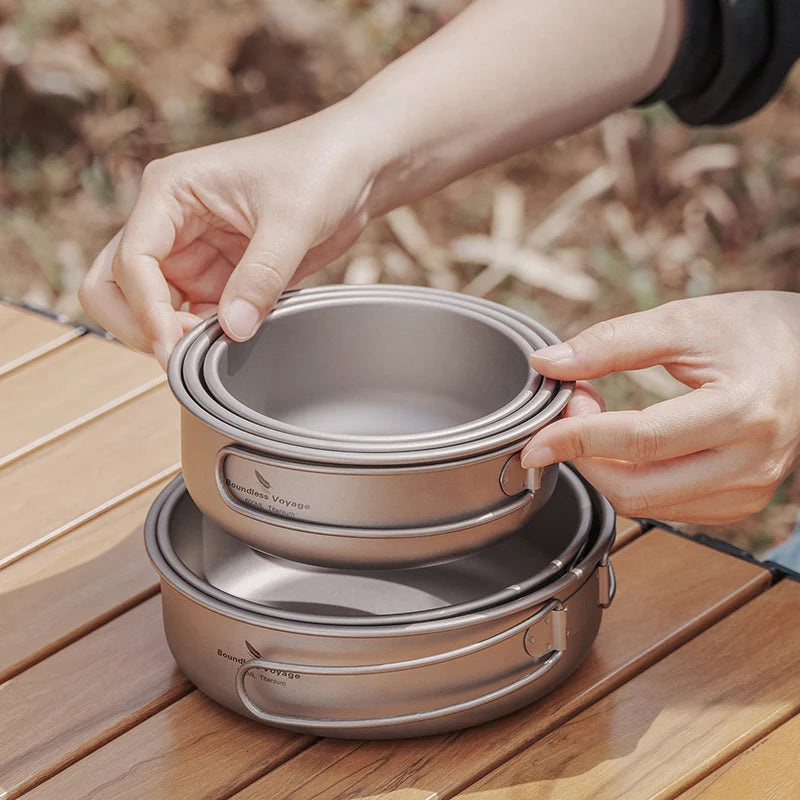 Stack of metal cookware on a wooden surface with hands holding the topmost pot.