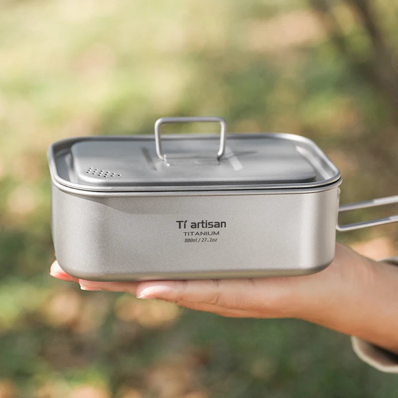 Titanium cooking pot held by a person with a blurred natural background