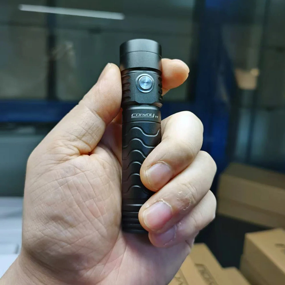 Hand holding a black flashlight with 'Convoy' branding against a blurred indoor background