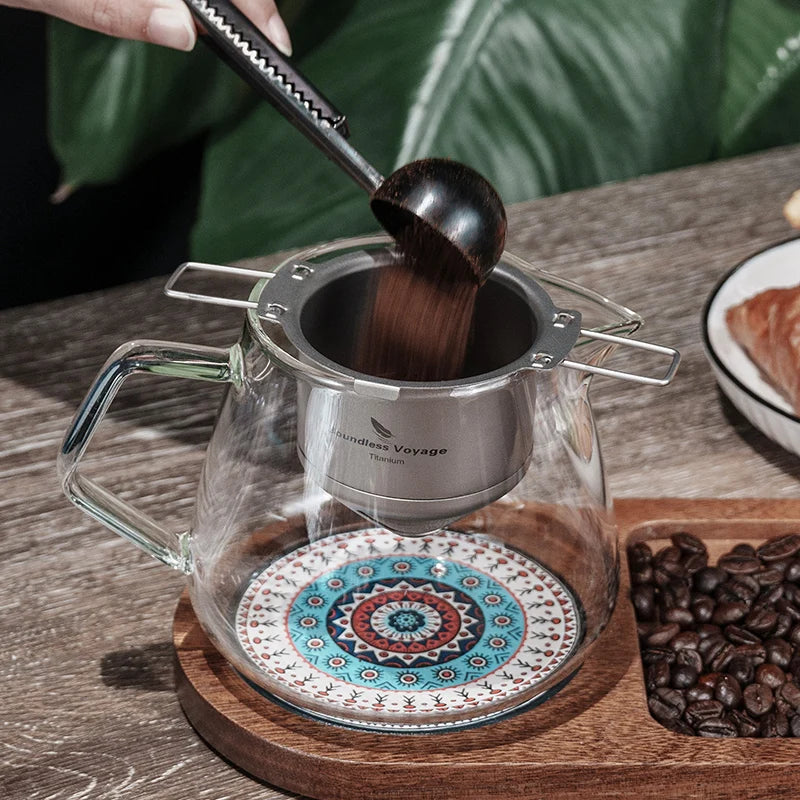 Coffee brewing setup with glass pot and mandala coaster on a wooden surface.