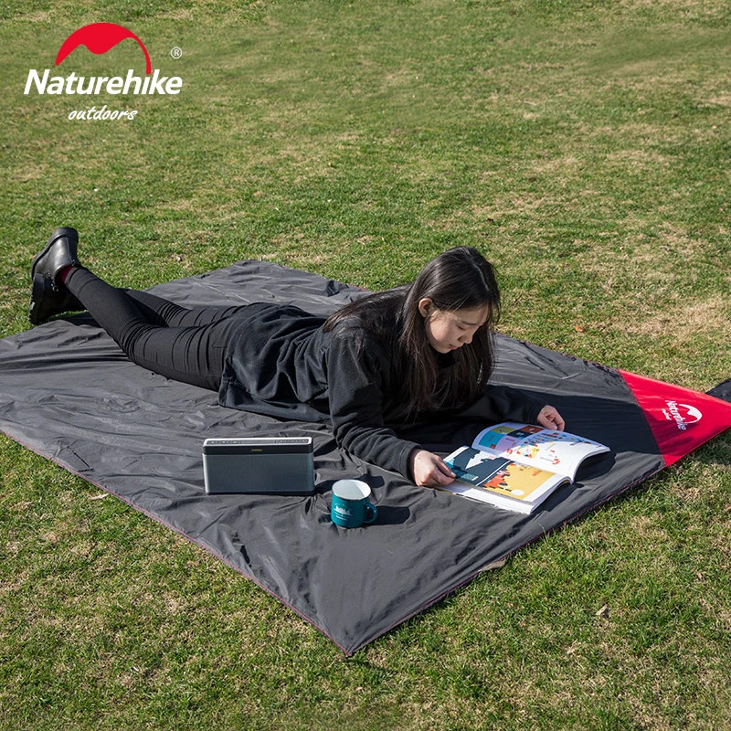 Person lying on a large gray outdoor blanket reading a book with a Naturehike logo in the corner.