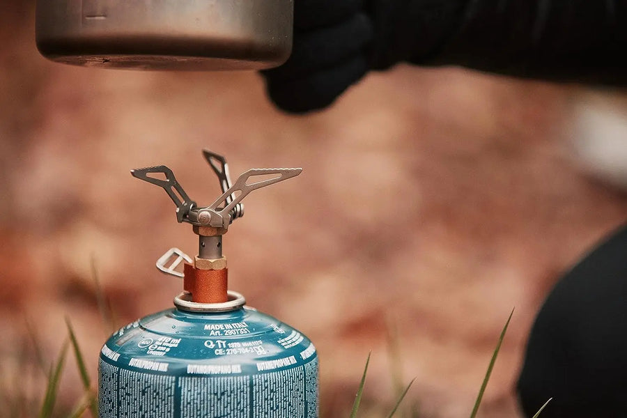 Close-up of a camping stove with a gas canister, blurred natural background