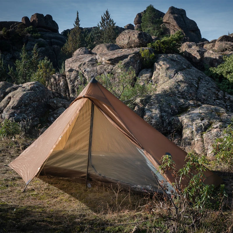 Brown tent pitched on a rocky landscape with trees and clear sky
