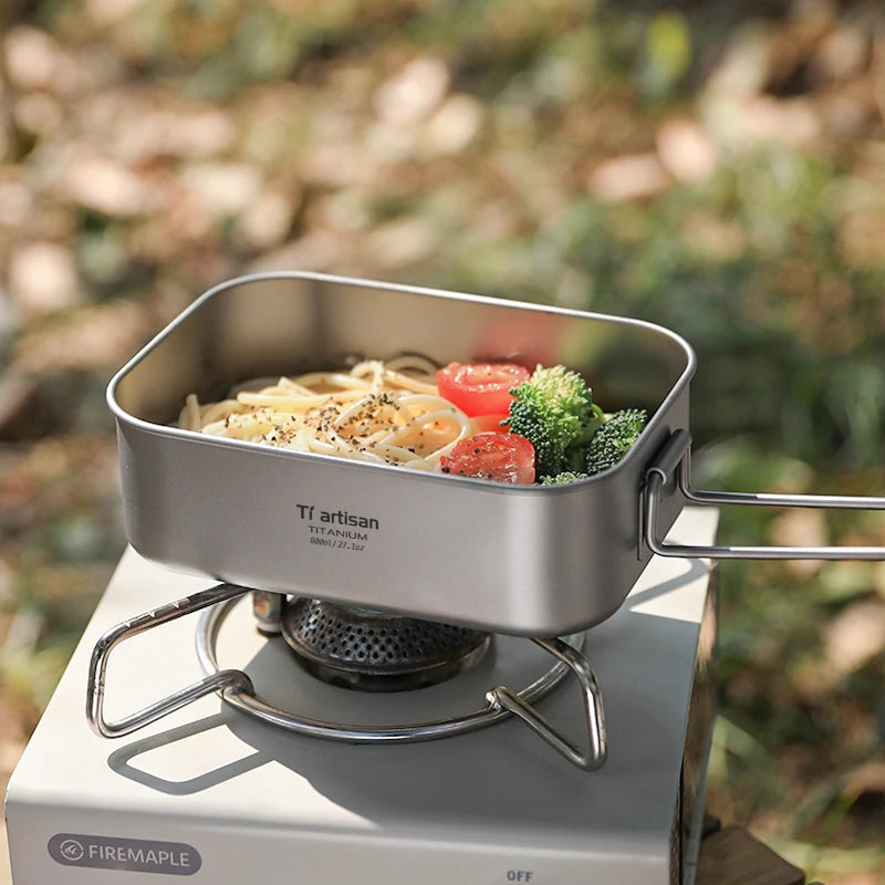 Portable stove with a pot containing noodles, tomatoes, and broccoli outdoors.
