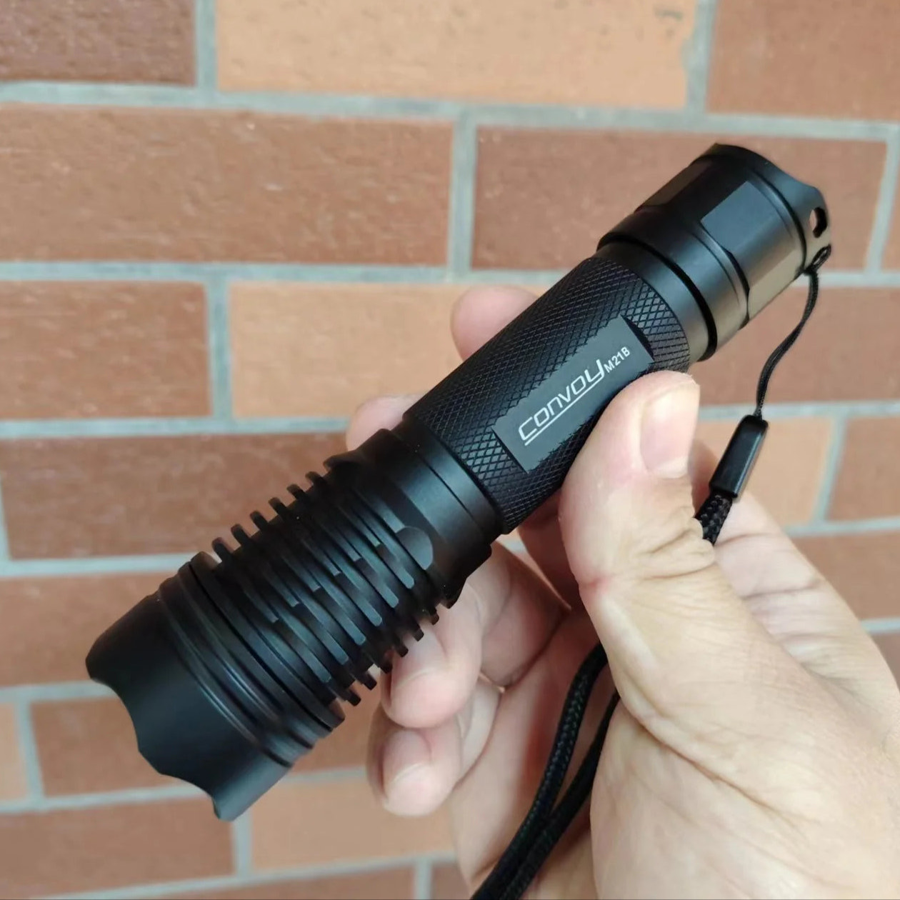 Black flashlight held in a hand with a brick wall background
