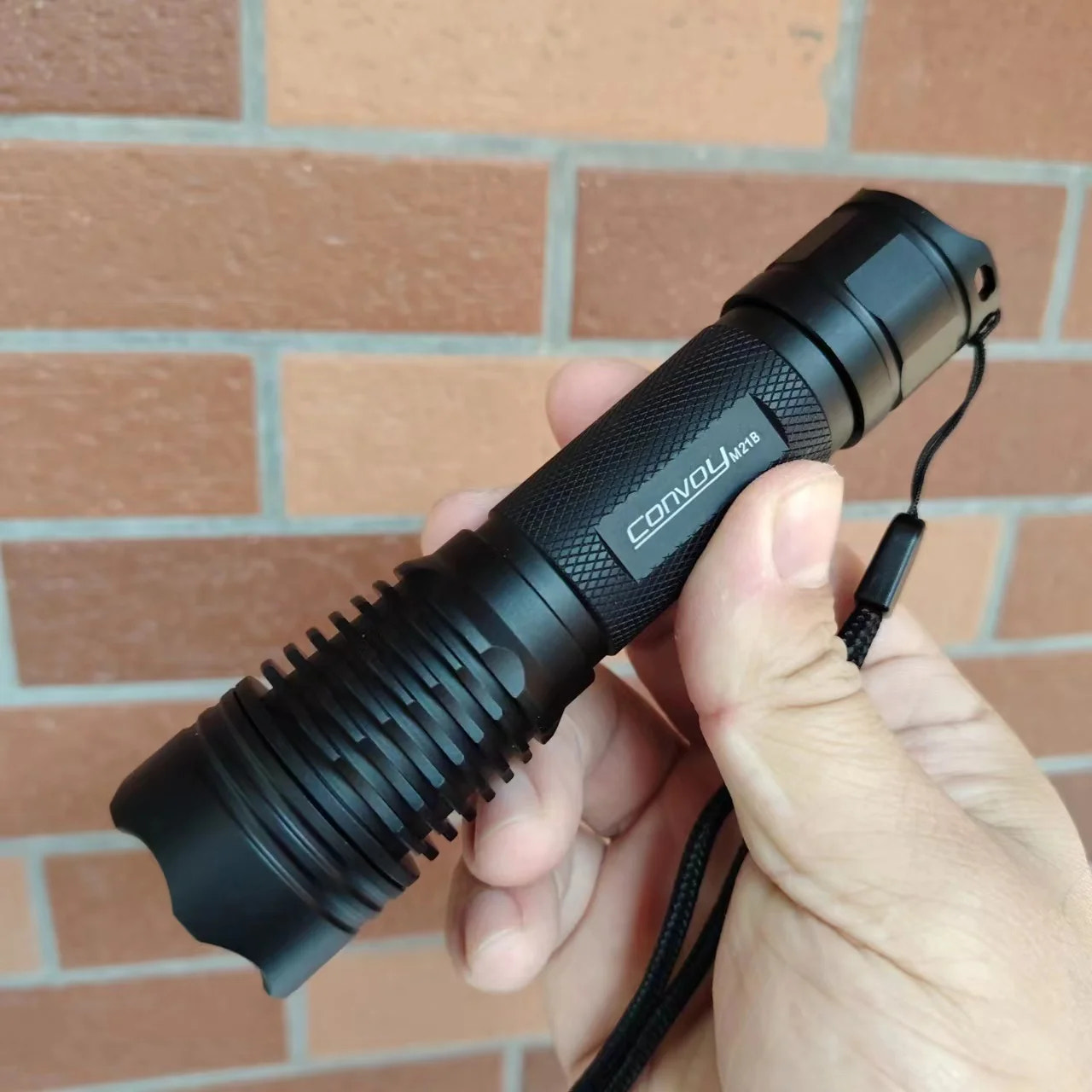 Black flashlight held in a hand with a brick wall background