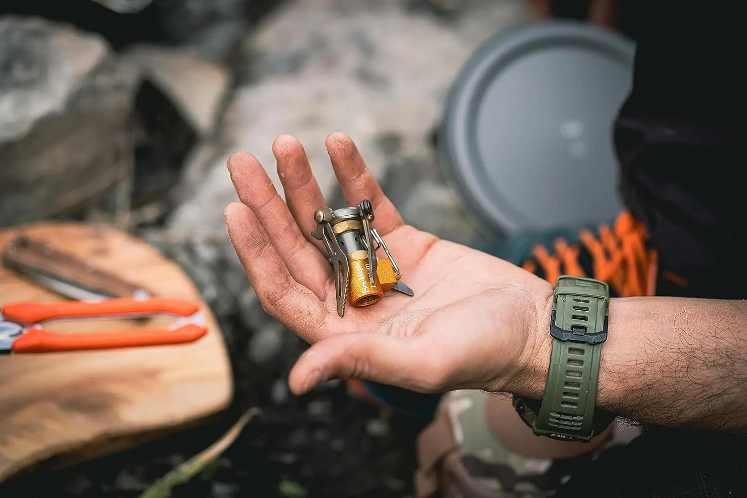 Hand holding a small camping stove with a blurred outdoor background