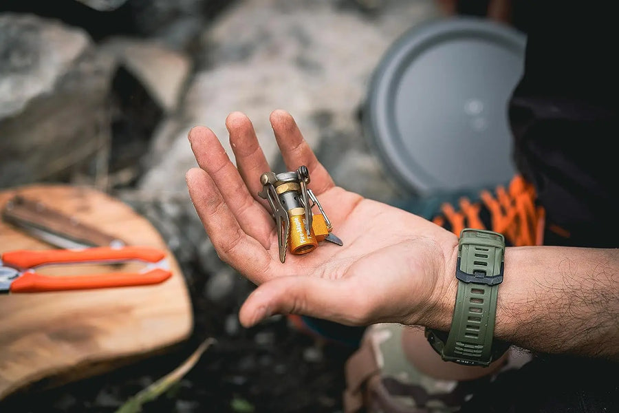 Hand holding a small camping stove with a blurred outdoor background