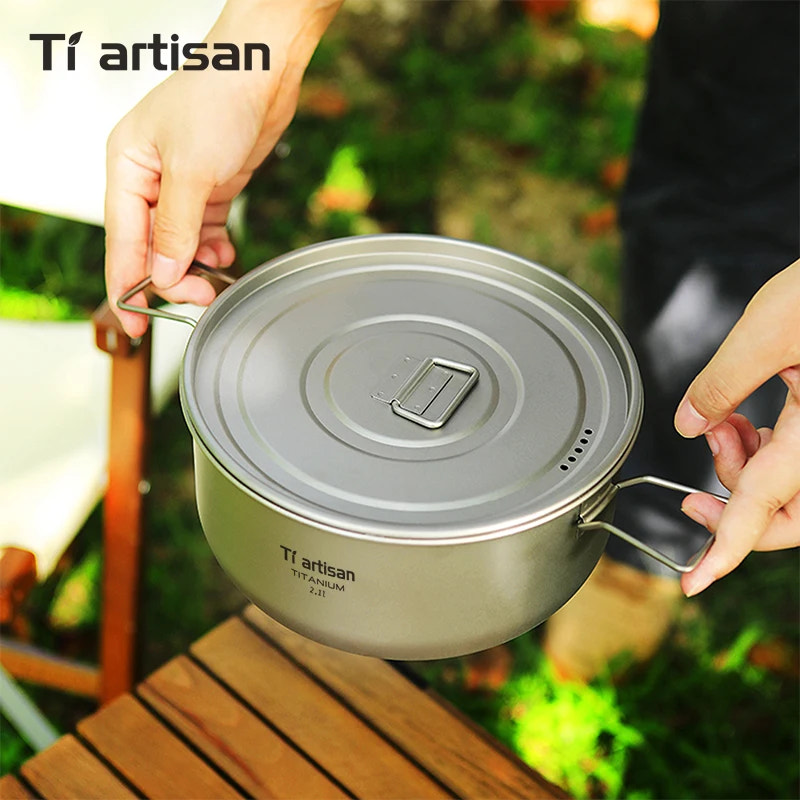 Titanium cookware with lid held by a person outdoors, featuring Tiartisan branding.