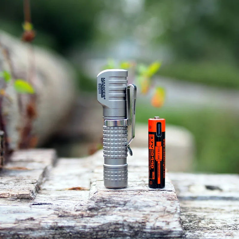 Silver flashlight and orange battery on a wooden surface with a blurred natural background