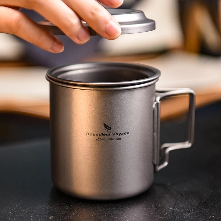 Titanium Cup with lid being held by a hand on a wooden surface.