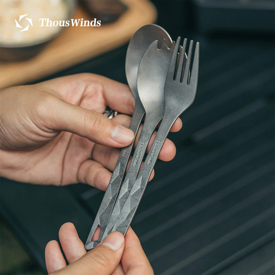 Person holding a set of ThousWinds camping cutlery on a grill background